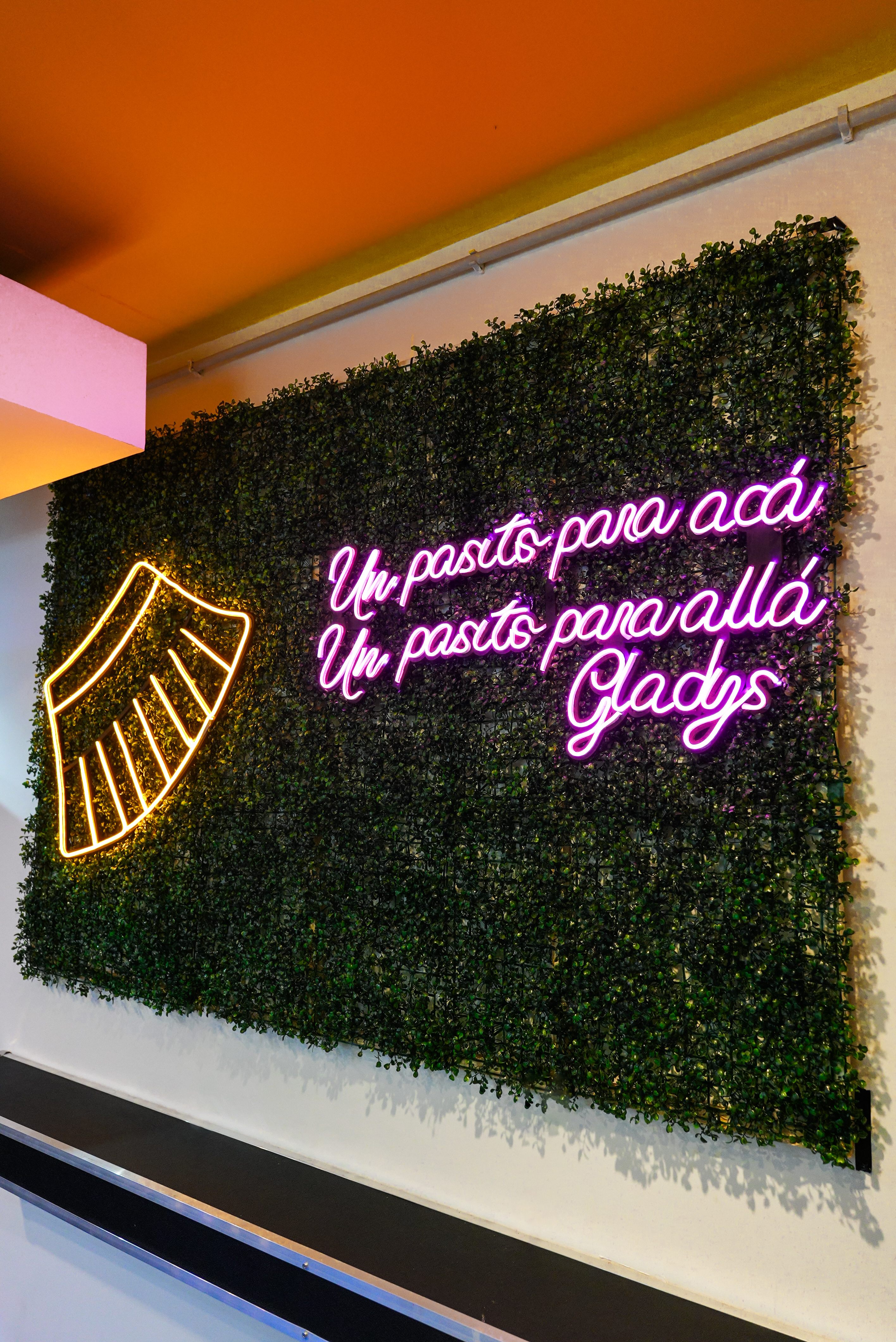 Cartel de neón con frase 'Un pasito para acá Un pasito para allá Gladys' y logo de empanada
